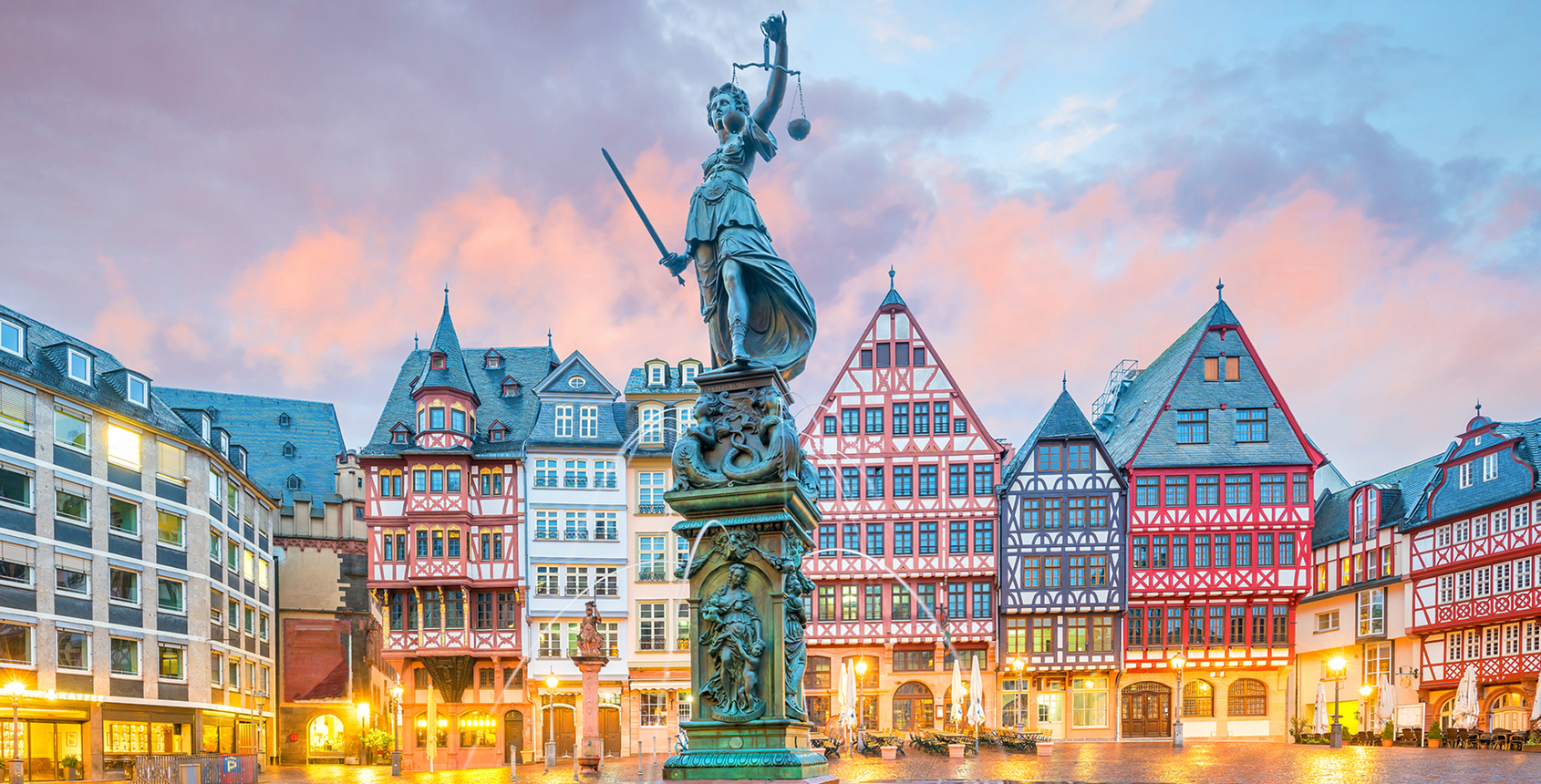 Historic statue in a vibrant town square at sunset.