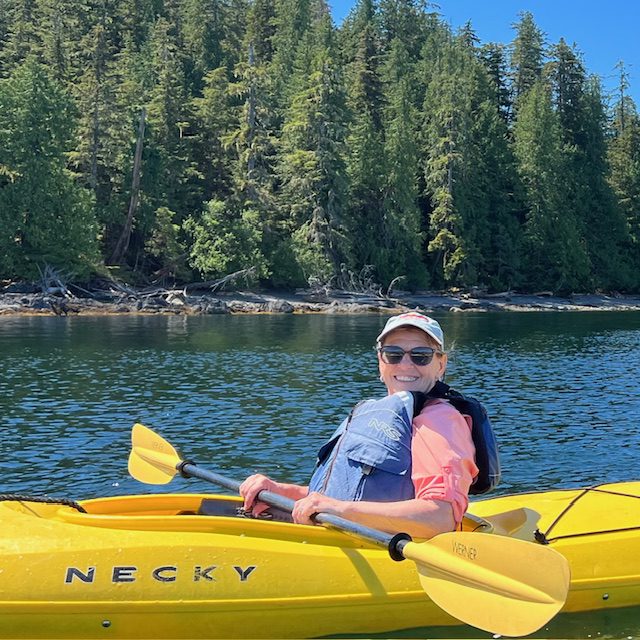 Person kayaking on a calm lake surrounded by forest.